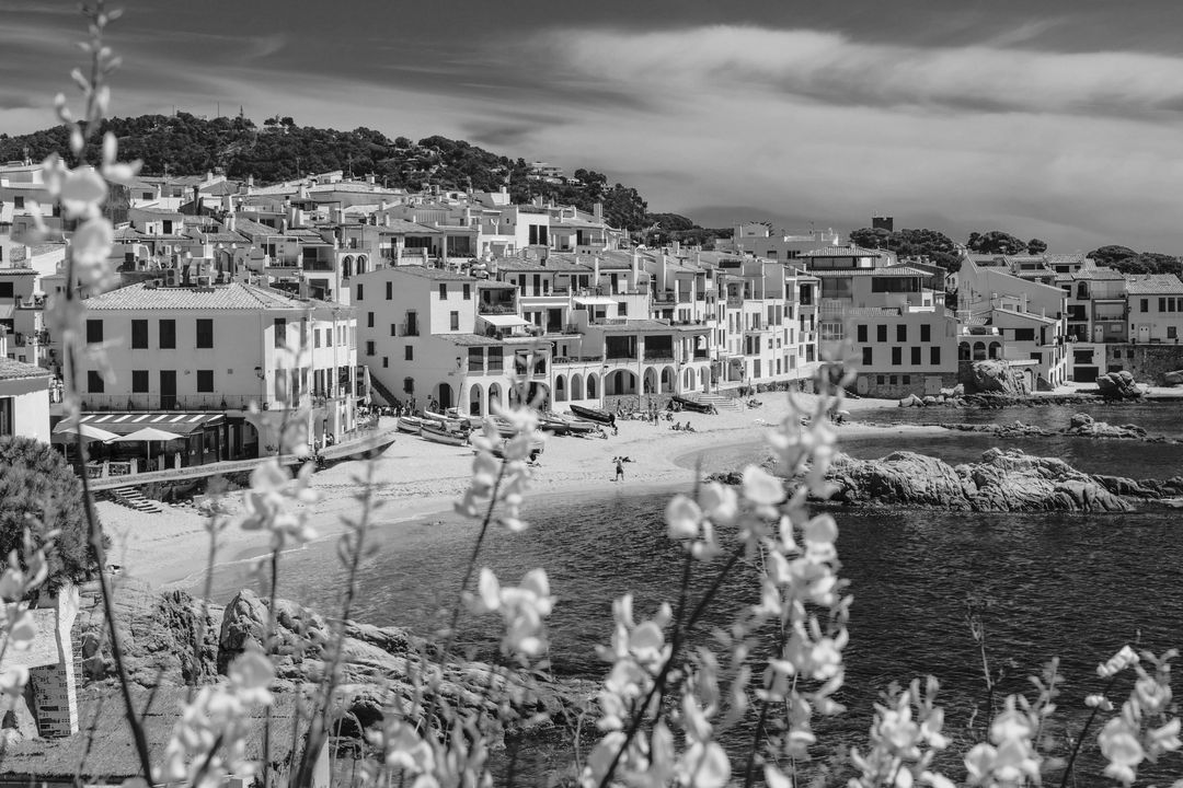 A white coastal village above a turquoise bay, framed by yellow flowers, edited by Ivo
